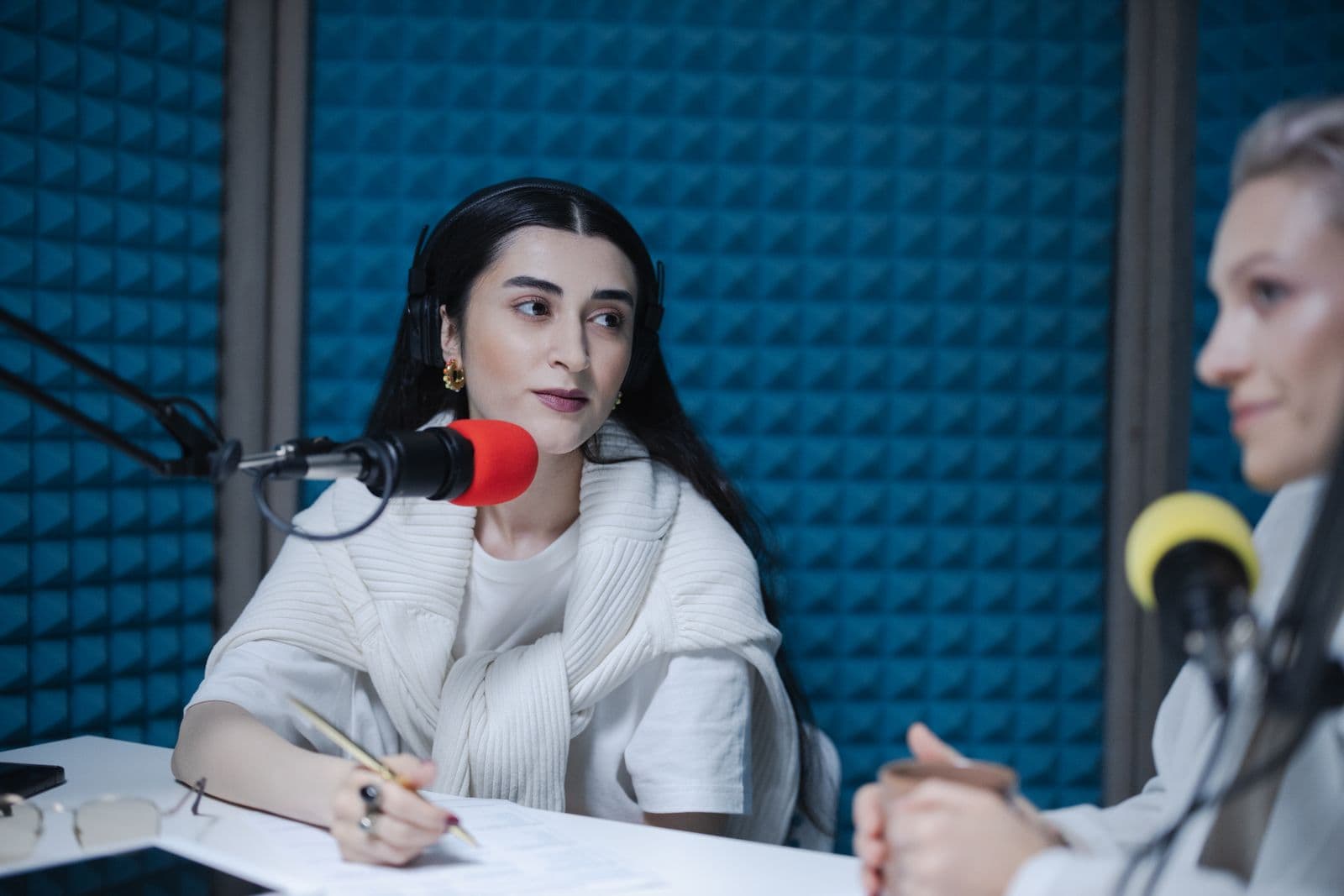 Two hosts recording a conversation in a podcast studio